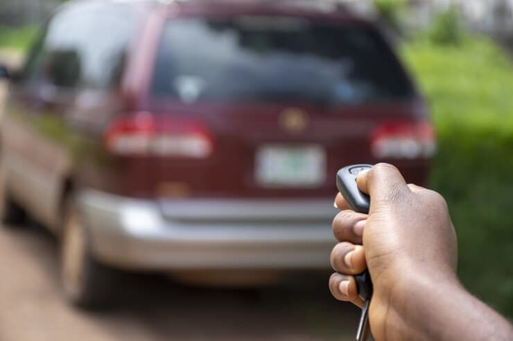 a hand using a car alarm remote control with a car in the background