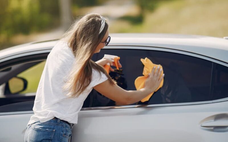 a woman wiping a car’s window with a dry yellow cloth
