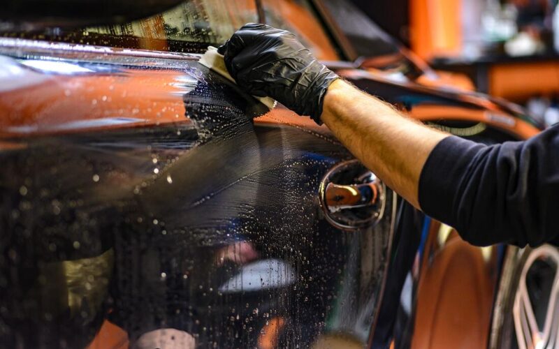 a man's hand waxes the surface of a car